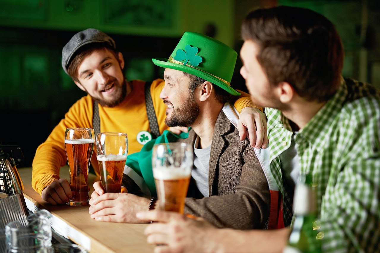 Three guys at a bar drinking pints dressed offensively 'Irish'