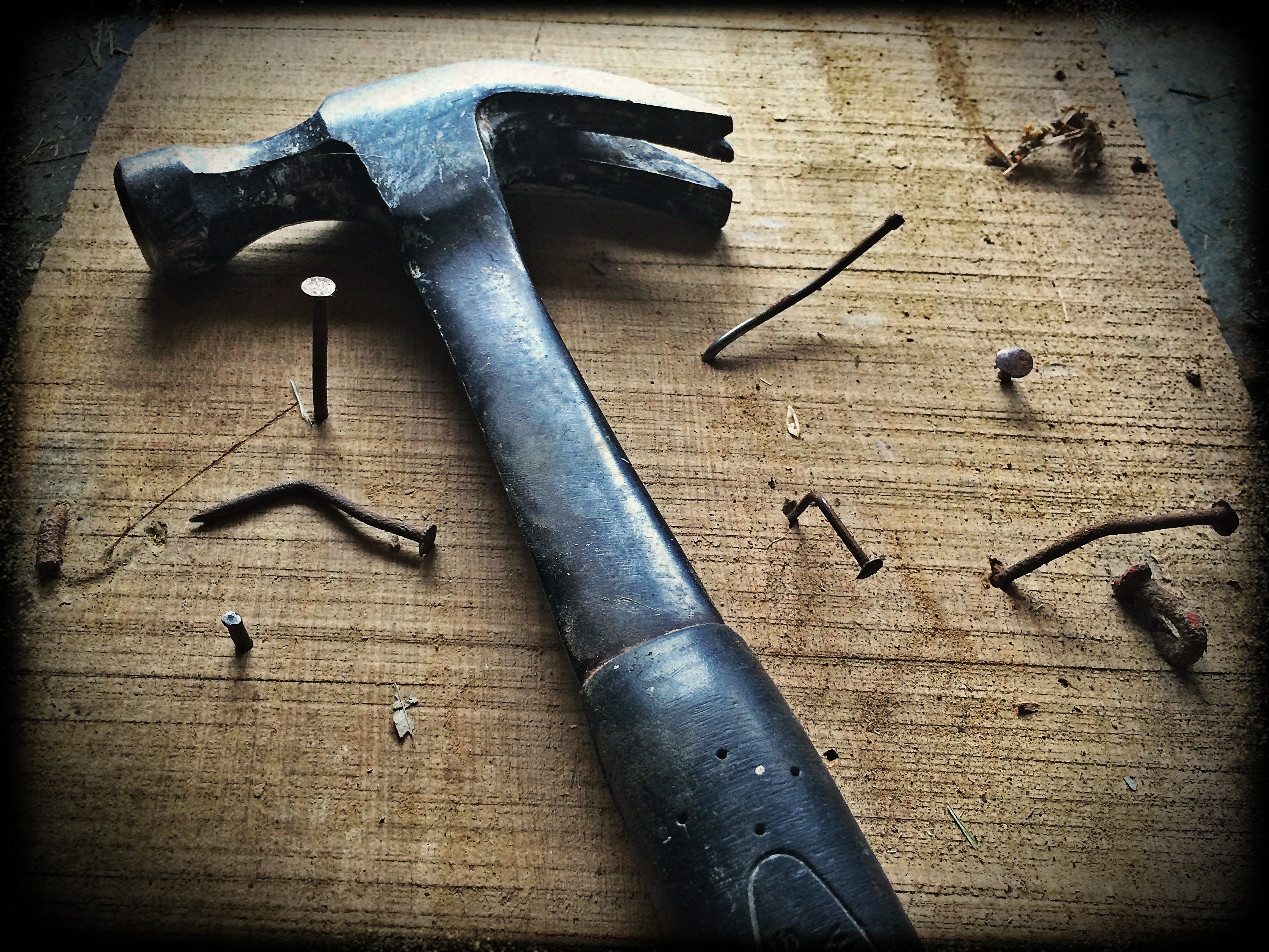 A hammer lying on a table surrounded by nails that were driven into the table with varying degrees of success